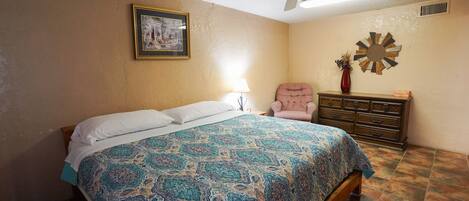 Une chambre à coucher comprenant un lit, un ventilateur de plafond, une commode et une horloge murale.