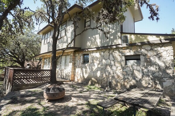 Un bâtiment en pierre de deux étages, doté d’une terrasse en bois, d’un foyer et d’une table de pique-nique.