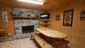 Un interior de madera con chimenea de piedra, un banco de madera, un televisor montado en la pared y obras de arte en las paredes.