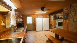 Una cocina compacta con armarios de madera, un refrigerador de doble puerta, una mesa de comedor y una chimenea de piedra.