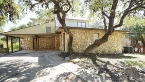Una casa de dos pisos con fachada de piedra, un porche cubierto y un árbol grande en frente.