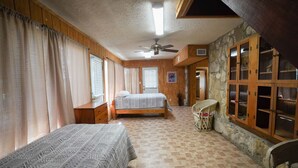 Un dormitorio con dos camas, ventilador de techo, paredes de madera y un detalle de pared de piedra.