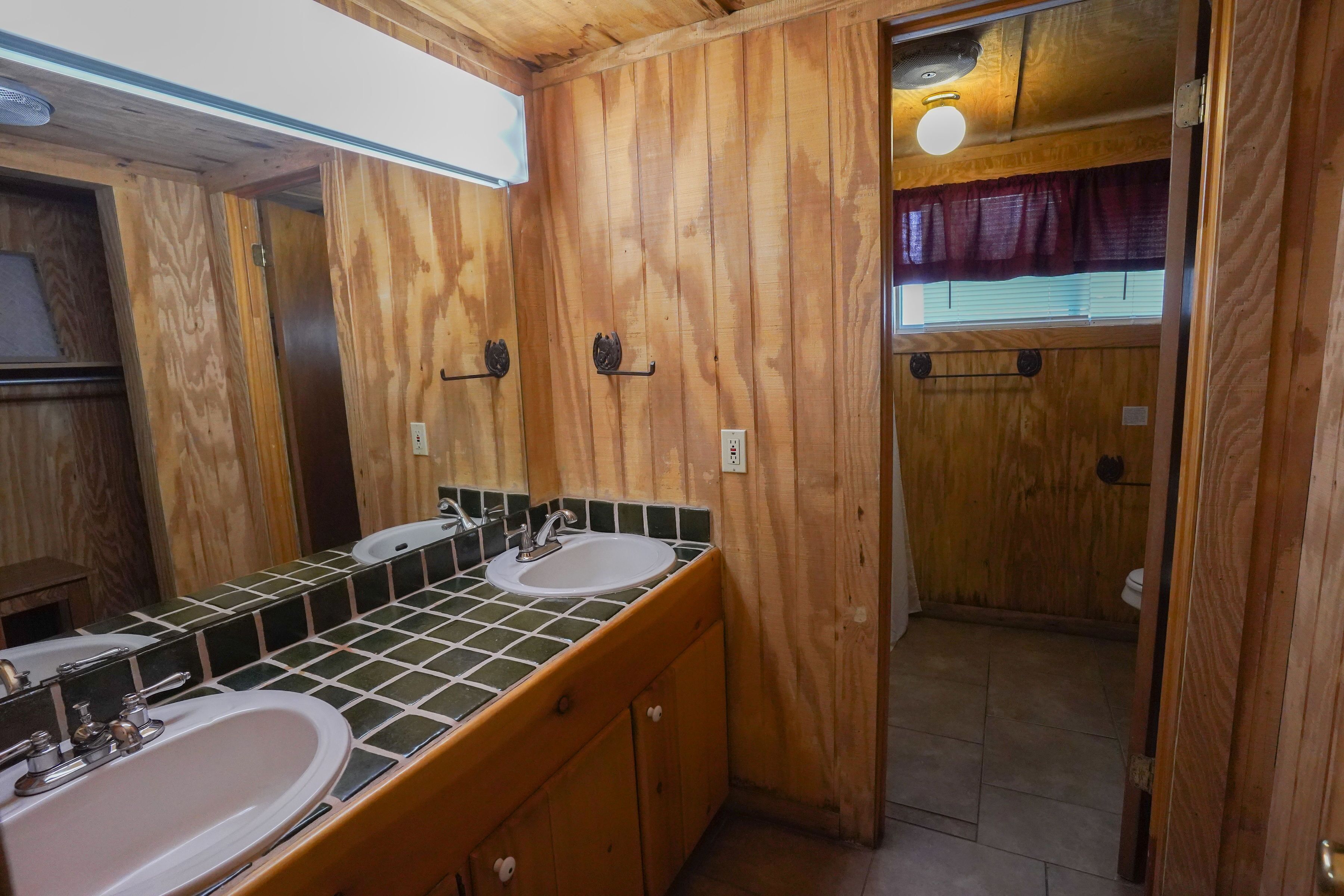 A wooden cabin bathroom with two sinks, a mirror, and a window with curtains.