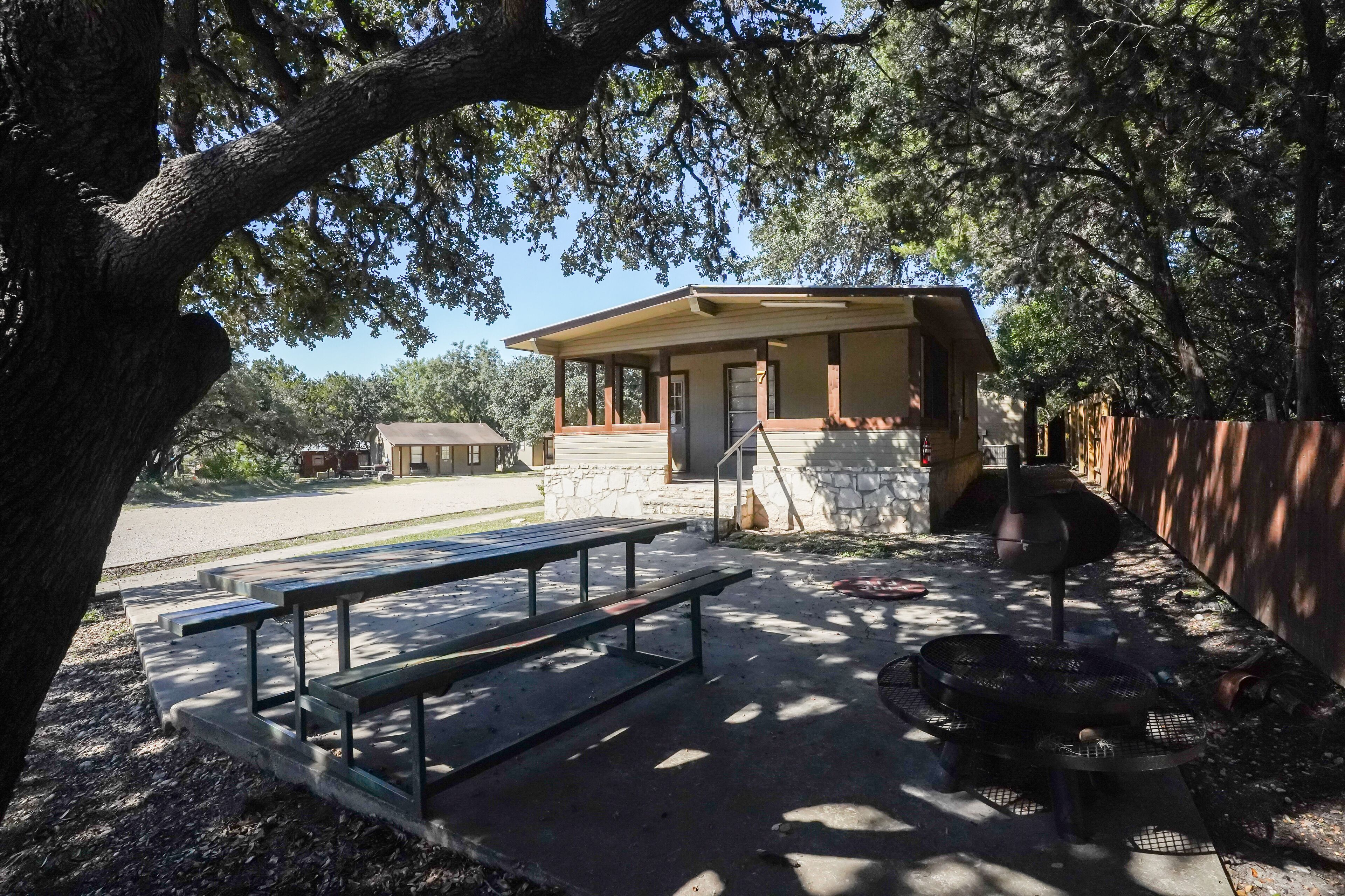 Un espace de pique-nique équipé de bancs et d’un barbecue, entouré d’arbres et délimité par un mur de pierres.