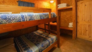 A bunk bed room with patterned bedding, a wooden wardrobe, and a shelf with towels. - Quaint cabin located near the Frio River (Concan)