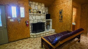 A cozy room with a stone fireplace, a bench, and a door with a window. - Quaint cabin located near the Frio River (Concan)