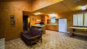 A compact kitchen with wooden walls and a checkered floor, a small dining area with a table and chairs, and a sofa. - Quaint cabin located near the Frio River (Concan)