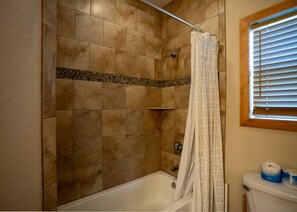 A bathroom with a shower, a toilet, and a window with blinds. - Nestled in Tierra Linda (Concan)