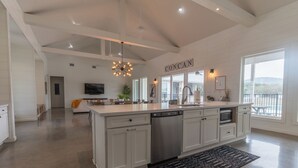 A spacious kitchen with white cabinetry, a central island, and a large window offering a view of the outdoors. - Unique Vacation Home located in Concan near the golf course (Concan)