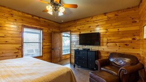 A wooden-paneled room with a bed, a leather chair, a TV, and a ceiling fan.