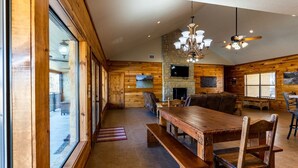 A spacious dining area with a wooden table and benches, a stone fireplace, and a television mounted on the wall.