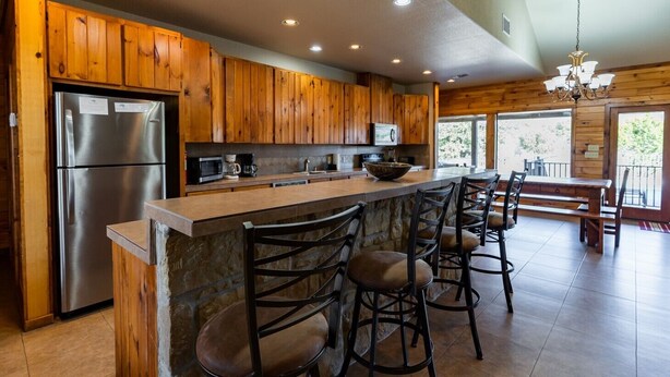 A kitchen with wooden cabinets, a stainless steel refrigerator, a microwave, and a large island with bar stools.