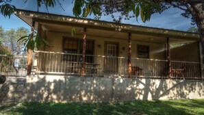 A two-story house with a porch, a stone wall, and a grassy yard. - River Front cabin with access to shared pool! (Concan)