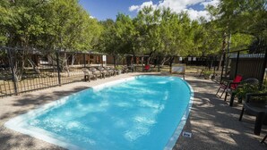 Una piscina rettangolare con bordo bianco, circondata da una recinzione nera. Sono presenti lettini e una sedia rossa vicino alla piscina.