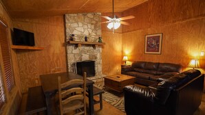 Una sala de estar acogedora con chimenea de piedra, sofá de cuero, mesa de madera y televisor montado en la pared.