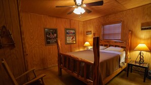 Un dormitorio de estilo rústico con una cama, dos lámparas de noche, una silla de madera y un ventilador de techo.