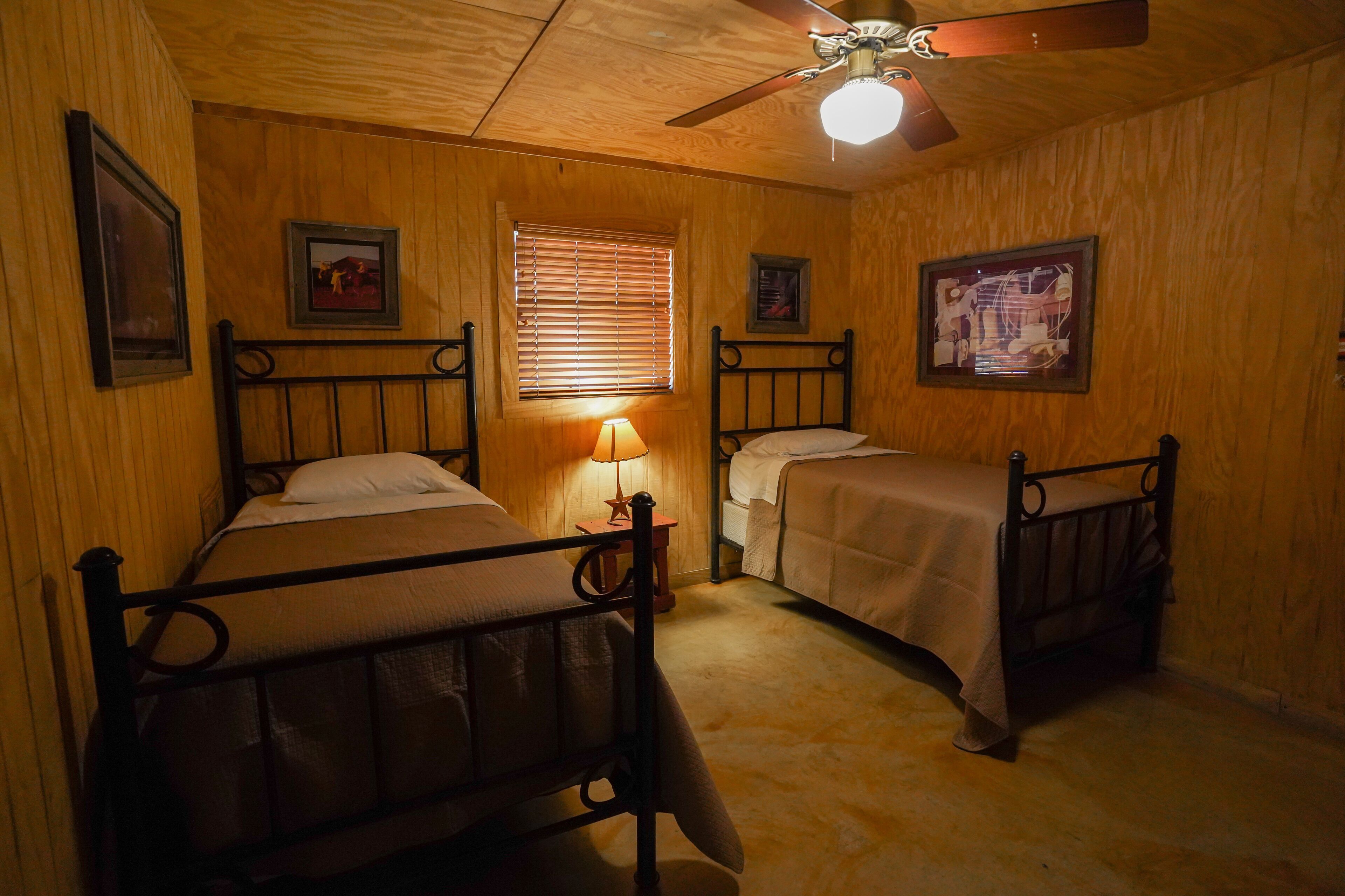 A room with two beds, wooden walls, a ceiling fan, and framed pictures on the walls.