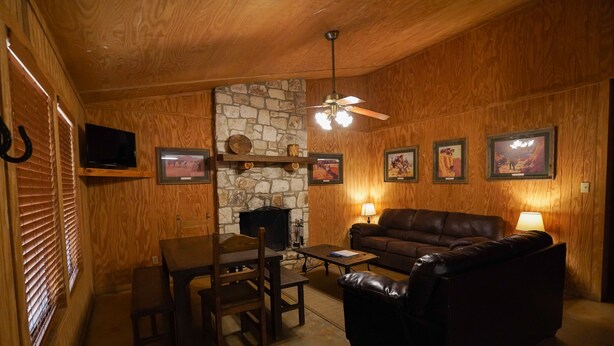 Ein gemütliches Wohnzimmer mit Kamin aus Stein, Holzwänden, einer Ledersofa, einem Esstisch mit Stühlen und gerahmten Bildern an der Wand.