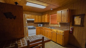 A compact kitchen with wooden cabinets, a microwave, a stove, and a window with blinds. - Walking distance to the Frio River, access to shared pool (Concan)