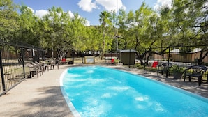 A rectangular swimming pool with a tiled edge, surrounded by a black metal fence. There are several lounge chairs and a red chair near the pool. - Walking distance to the Frio River, access to shared pool (Concan)