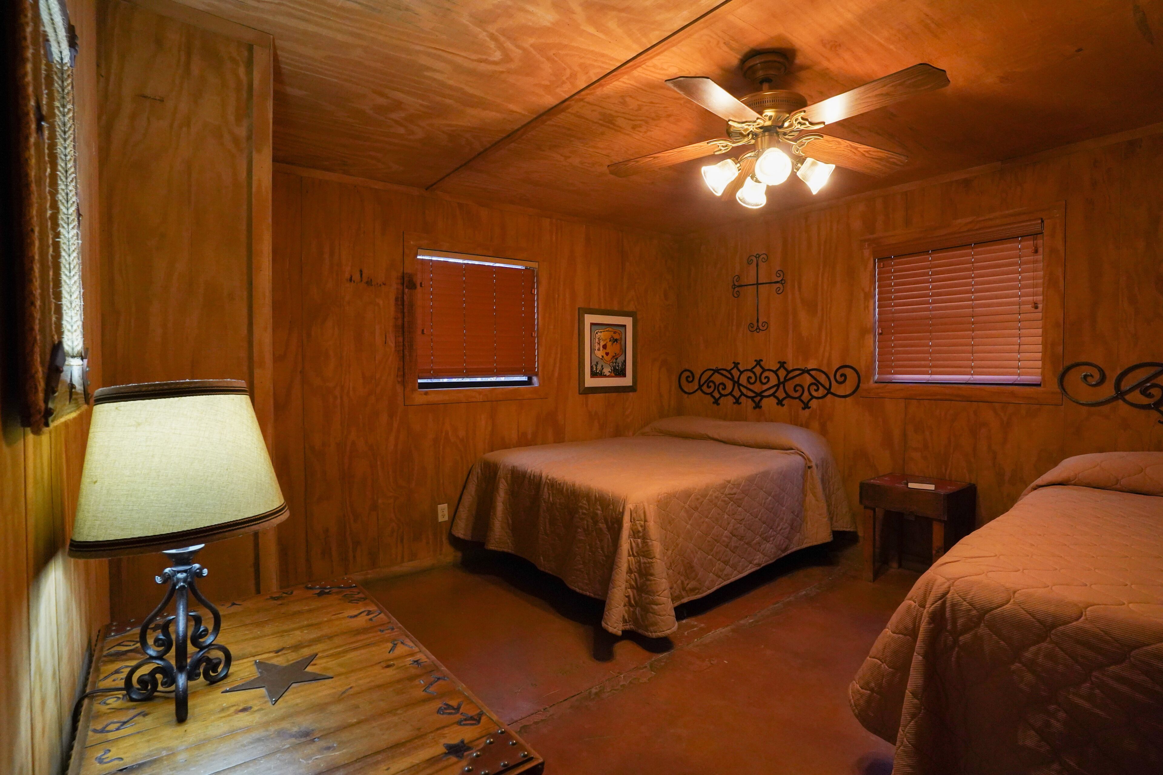 A wooden room with two beds, a ceiling fan, and a lamp.