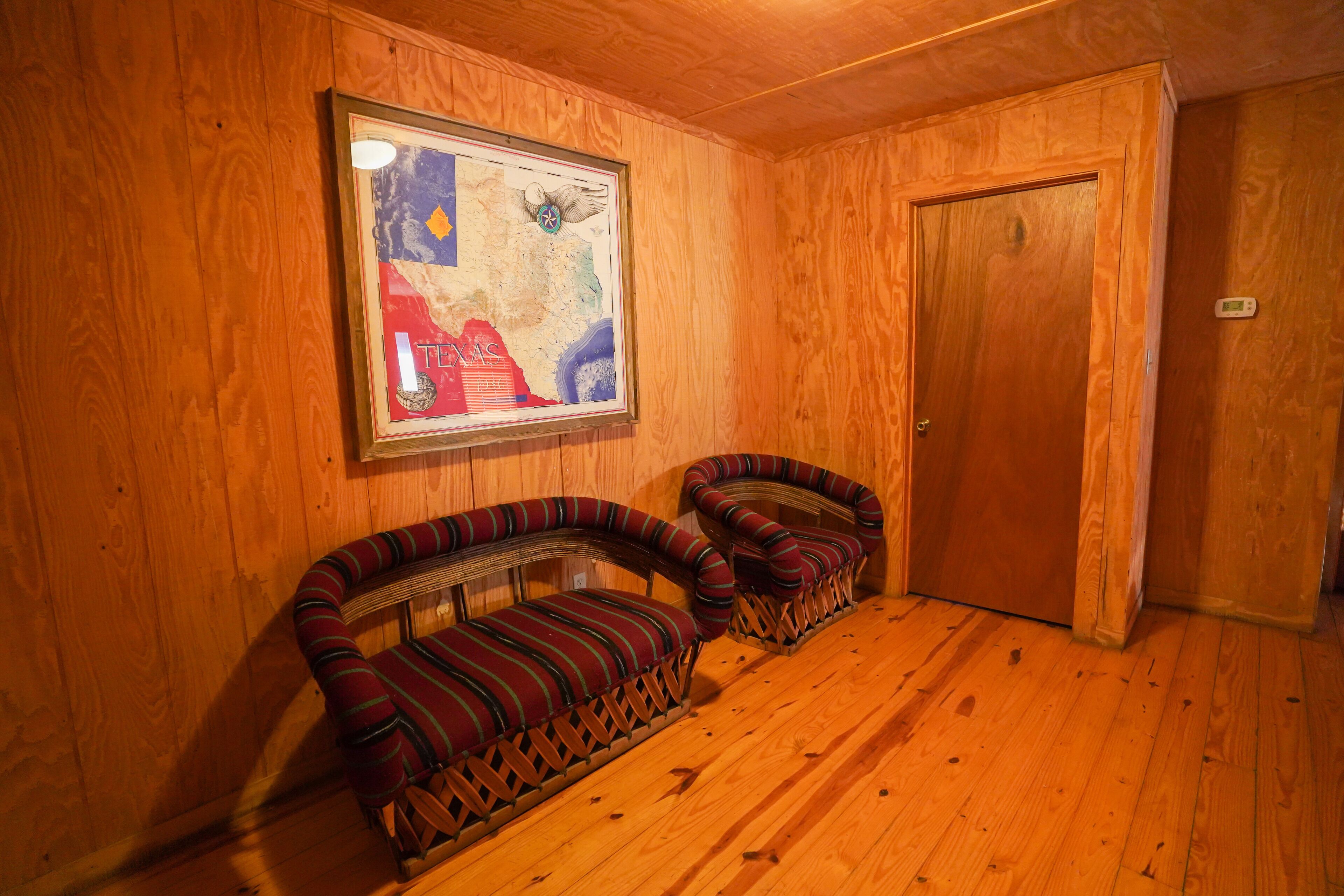 A wooden interior with two upholstered chairs, a framed map on the wall, and a wooden door.