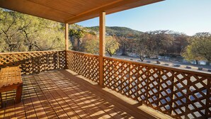 Eine Holzterrasse mit Gittergeländer, einer Bank und Blick auf einen Fluss und Hügel.