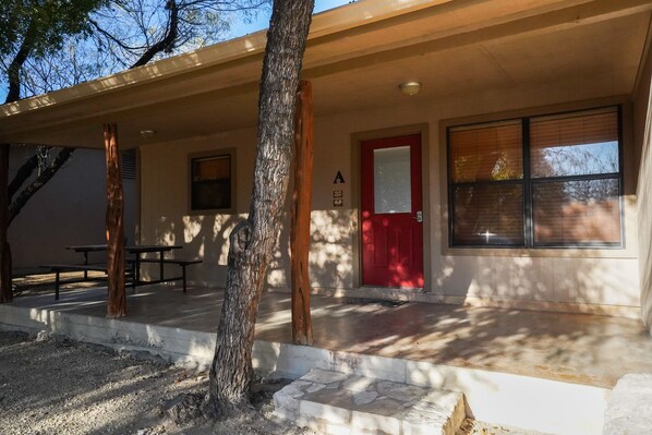 A building with a red door, a window with blinds, and a picnic table outside. - Riverfront cabin with a pool! (Concan)