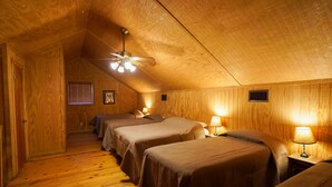 Una habitación de madera con tres camas, un ventilador de techo y una ventana con persianas.