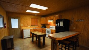 Una cocina con armarios de madera, una mesa de madera, un refrigerador y un microondas.