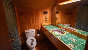 Bany d'estil cabana de fusta amb vàter, un lavabo amb mirall i zona de dutxa.