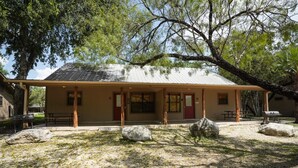 A rustic building with a covered porch, large rocks, and a picnic table. - Riverfront cabin with access to shared pool! (Concan)
