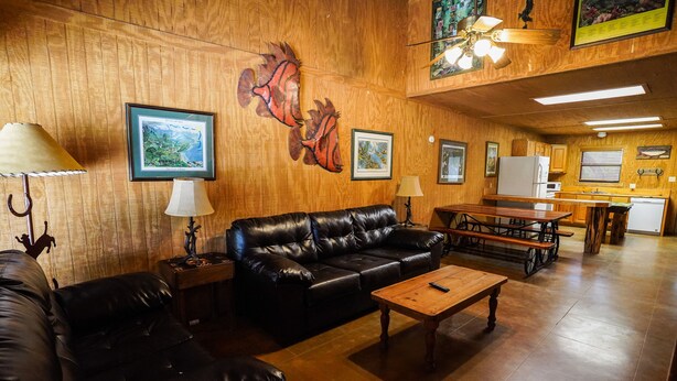 A cozy living room with a leather sofa, wooden coffee table, and a dining area with a wooden table and chairs. - Riverfront cabin with access to shared pool! (Concan)