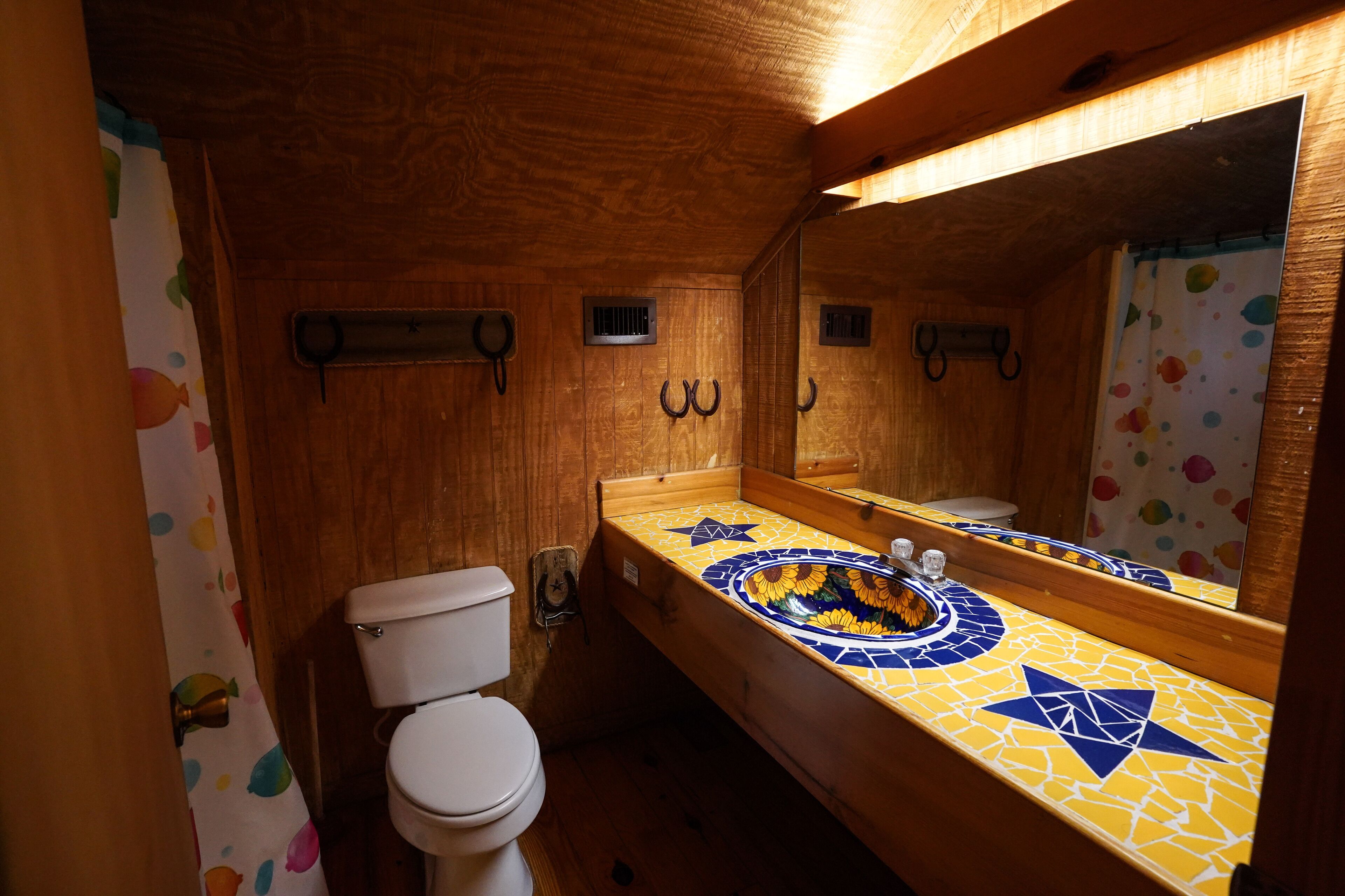 A wooden bathroom with a toilet, a sink with a mosaic countertop, and a mirror.