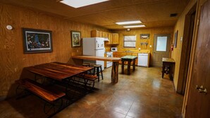 A compact kitchen with wooden cabinets, a refrigerator, a microwave, and a dining area with benches. - Riverfront cabin with access to shared pool! (Concan)