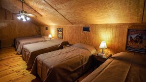 A cozy room with wooden walls and floors, featuring two beds with headboards, a ceiling fan, and a poster on the wall. - Riverfront cabin with access to shared pool! (Concan)