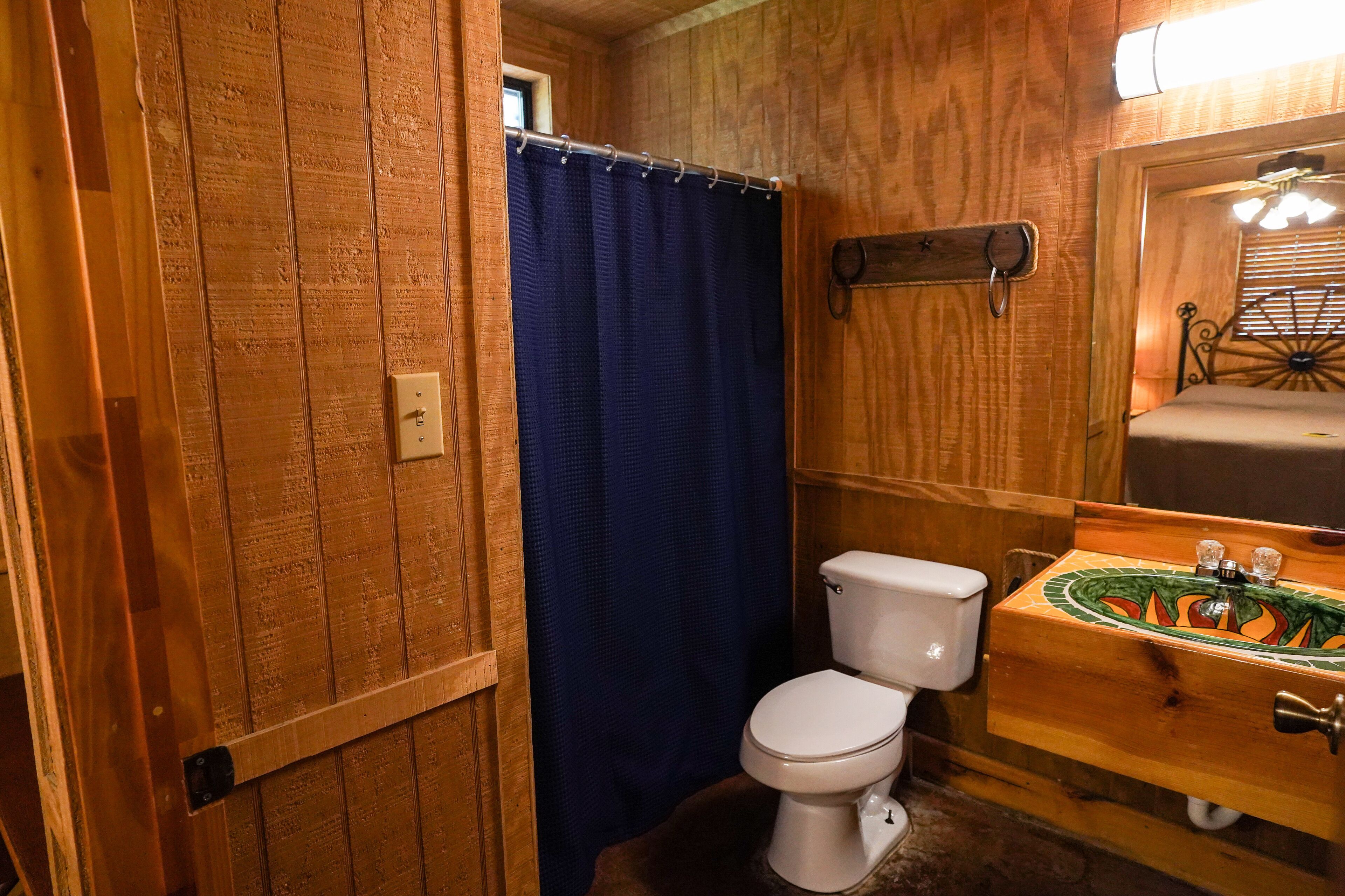 A wooden-paneled bathroom with a white toilet, a blue shower curtain, and a wooden sink with a decorative tile backsplash.