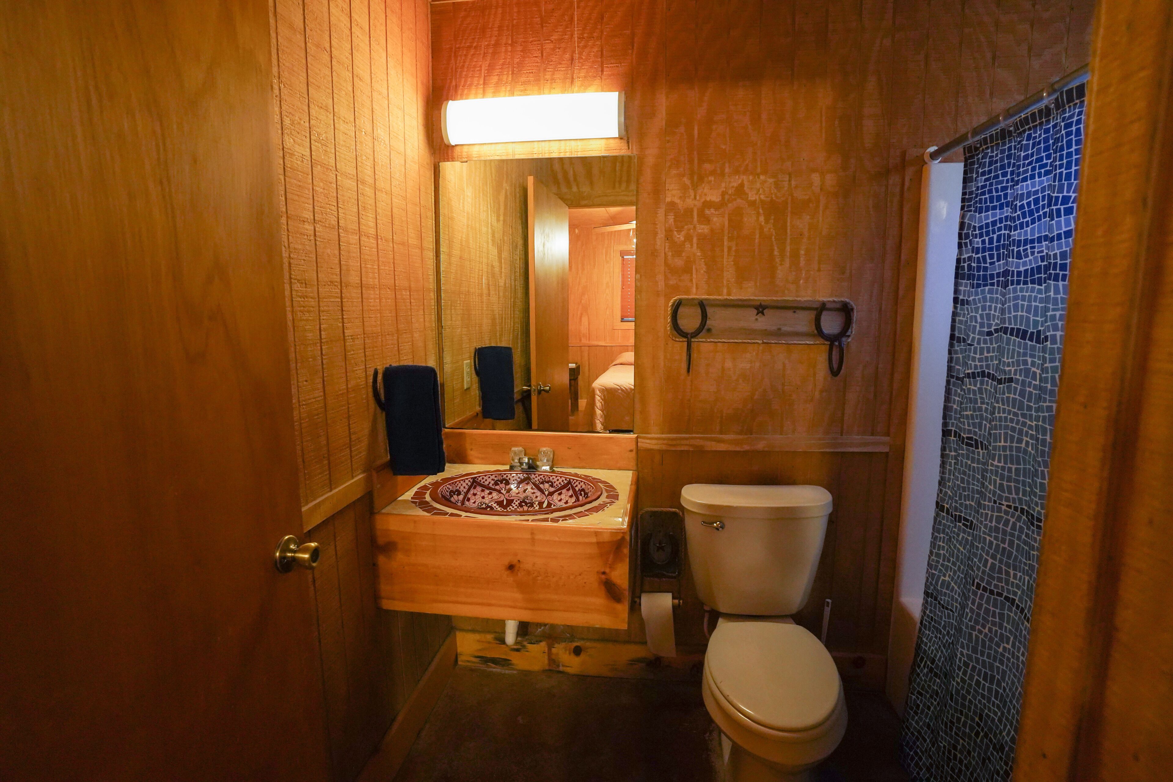 A compact bathroom with a wooden sink, toilet, and a mosaic shower enclosure.