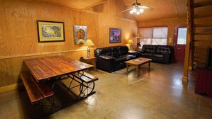 A wooden interior with a wooden table, benches, a black leather sofa, and a ceiling fan. - Riverfront cabin with access to shared pool! (Concan)