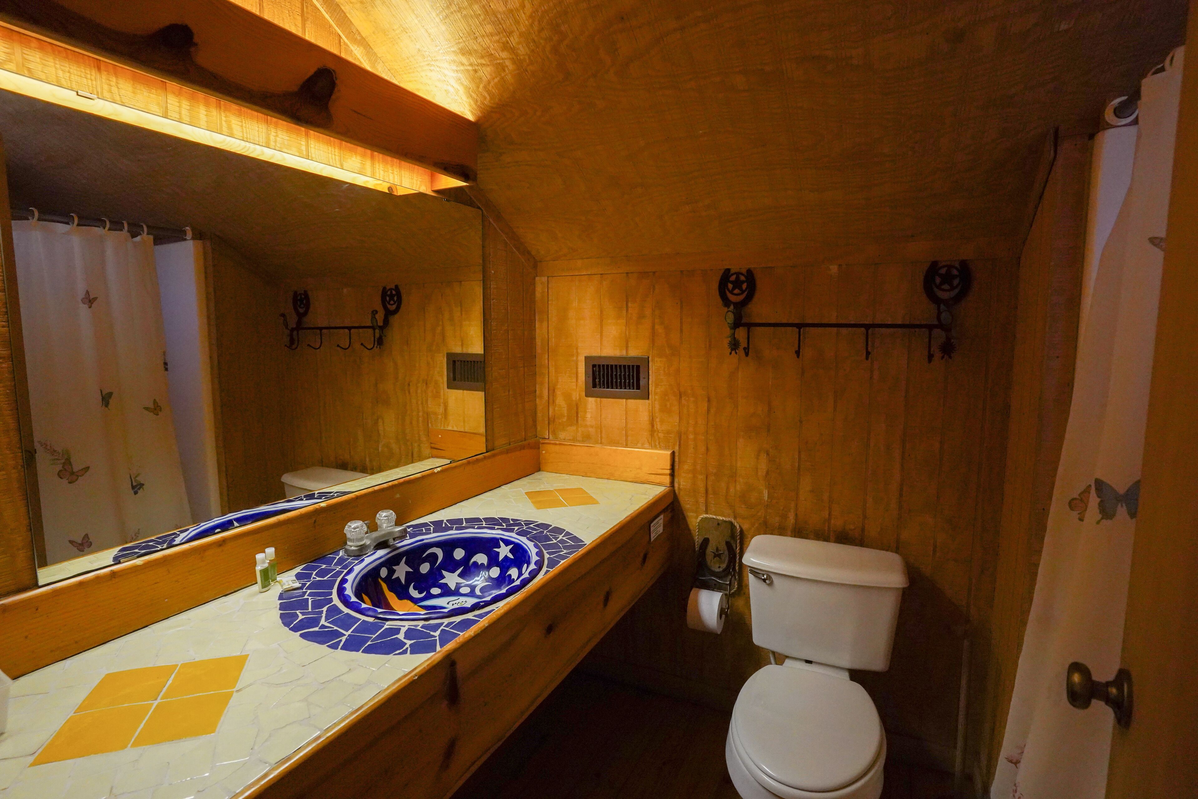 A wooden interior bathroom with a large mirror, a sink with a decorative tile backsplash, and a toilet.