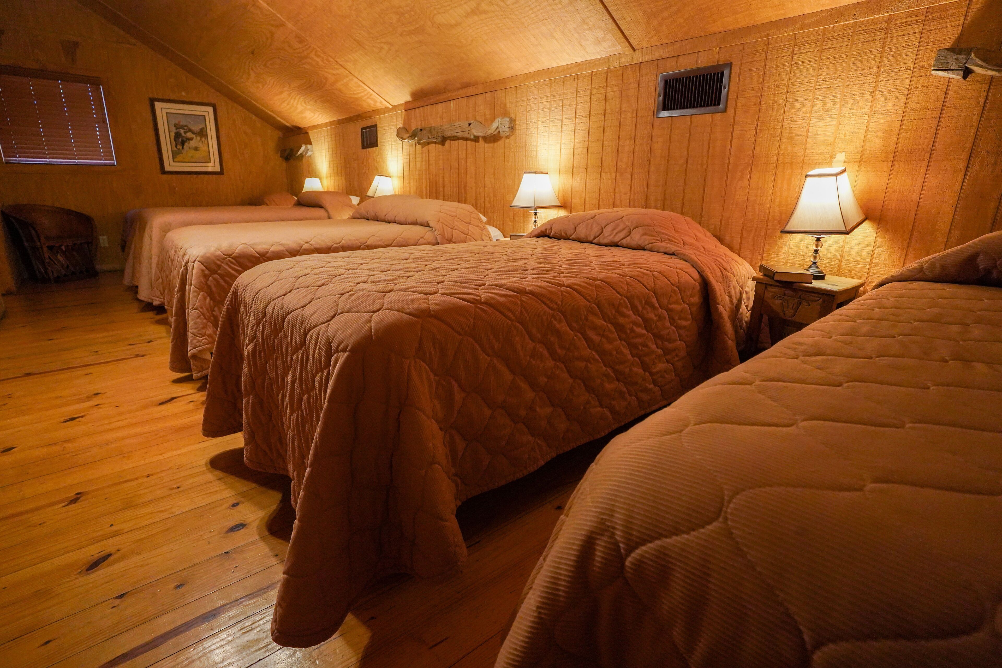 A room with four beds, wooden walls, and a sloped ceiling.