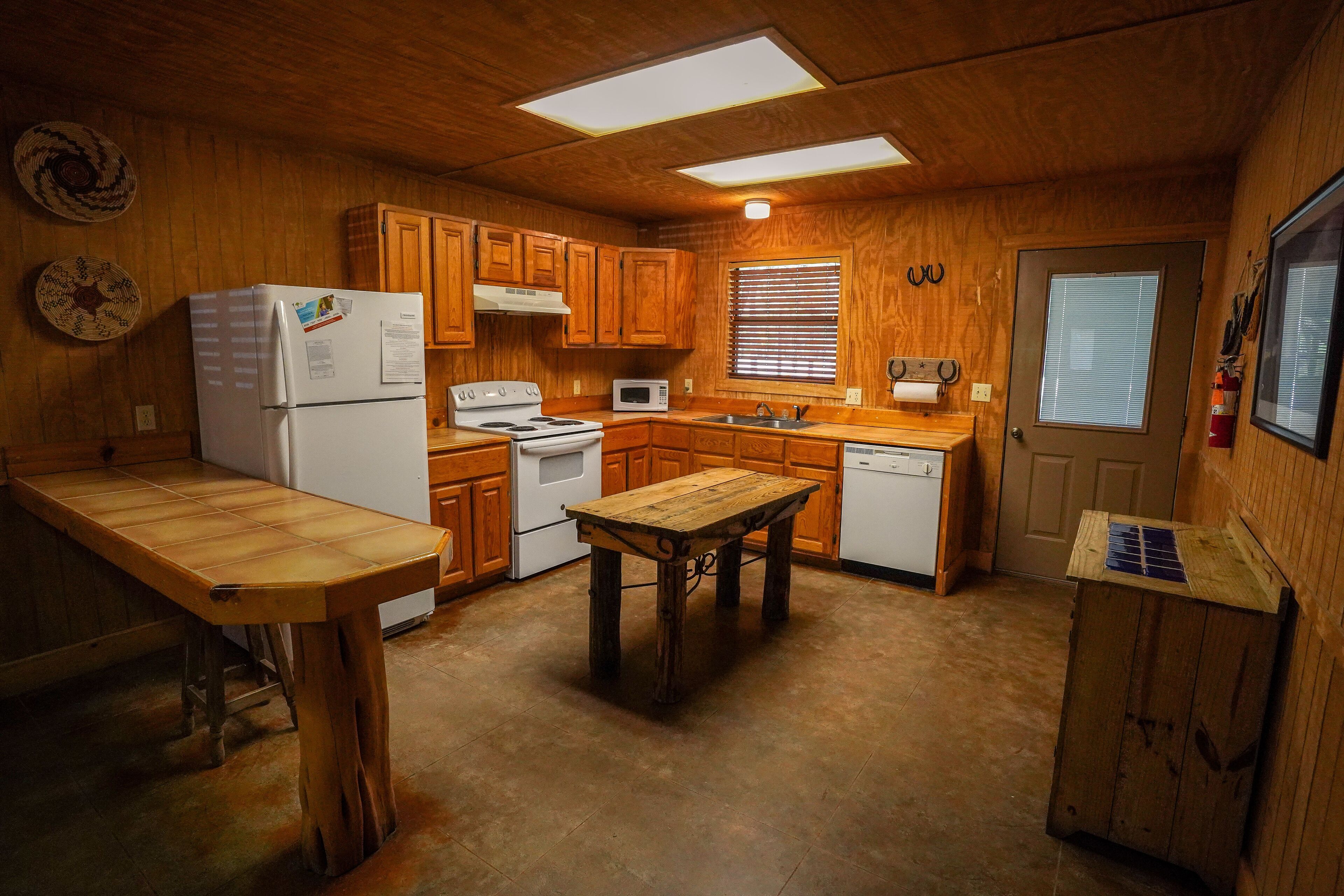 Une cuisine compacte avec des meubles de rangement en bois, un réfrigérateur, une cuisinière, un four à micro-ondes et une table en bois.