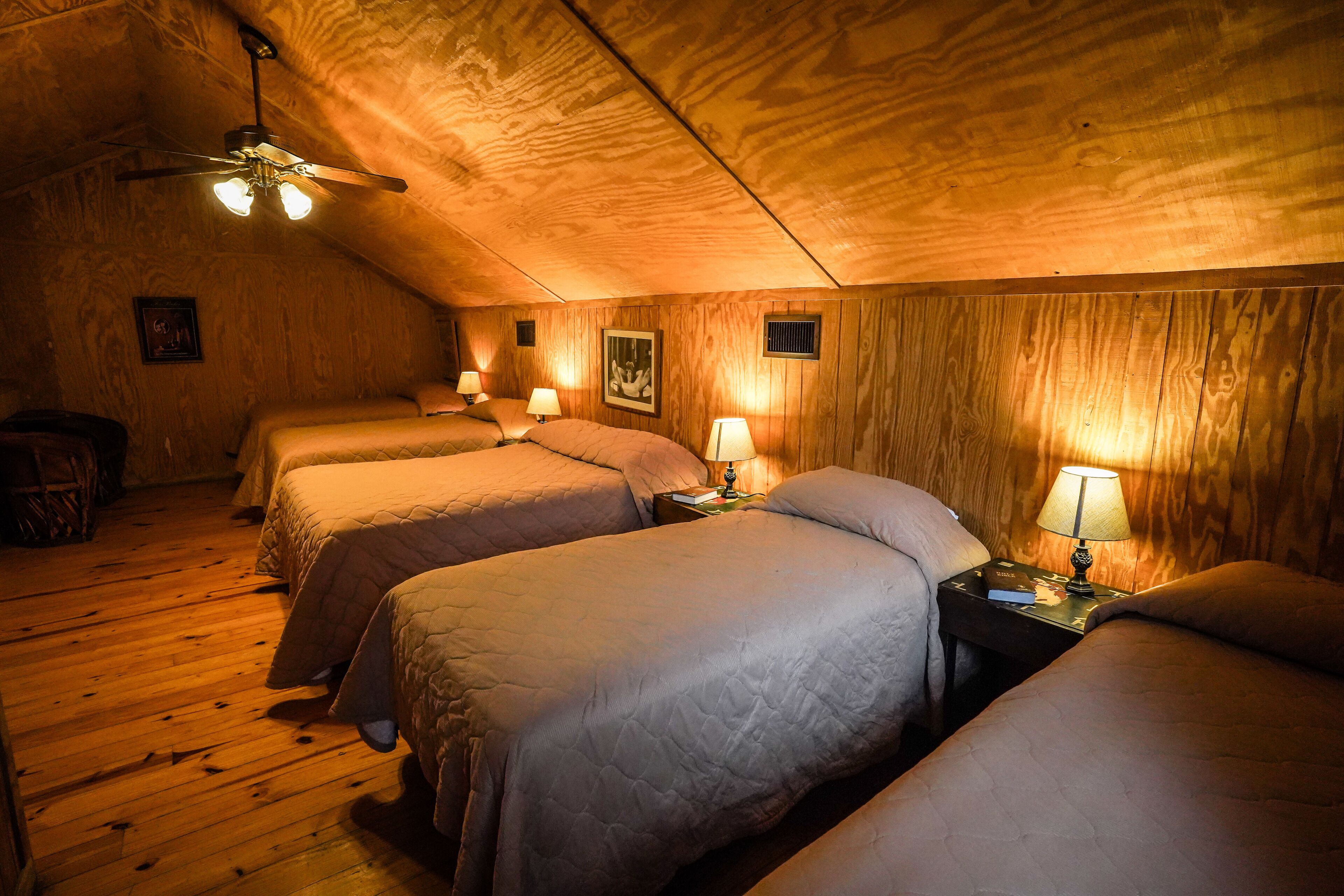 Une chambre confortable située dans les combles, avec trois lits, des murs en bois et un ventilateur de plafond.