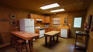 A kitchen with wooden cabinets, a refrigerator, a microwave, a wooden table, and bar stools. - Riverfront cabin with access to shared pool! (Concan)