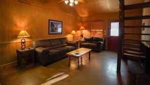 A cozy living room with wooden walls, a ceiling fan, and two couches. - Riverfront cabin with access to shared pool! (Concan)