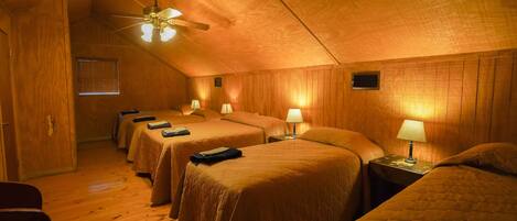 Quarto com quatro camas de solteiro, paredes de madeira, ventoinha no teto e janela com cortinas.