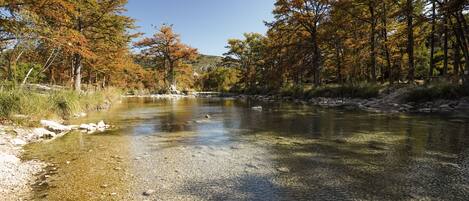 A clear river with a rocky bed, surrounded by trees with autumn foliage.