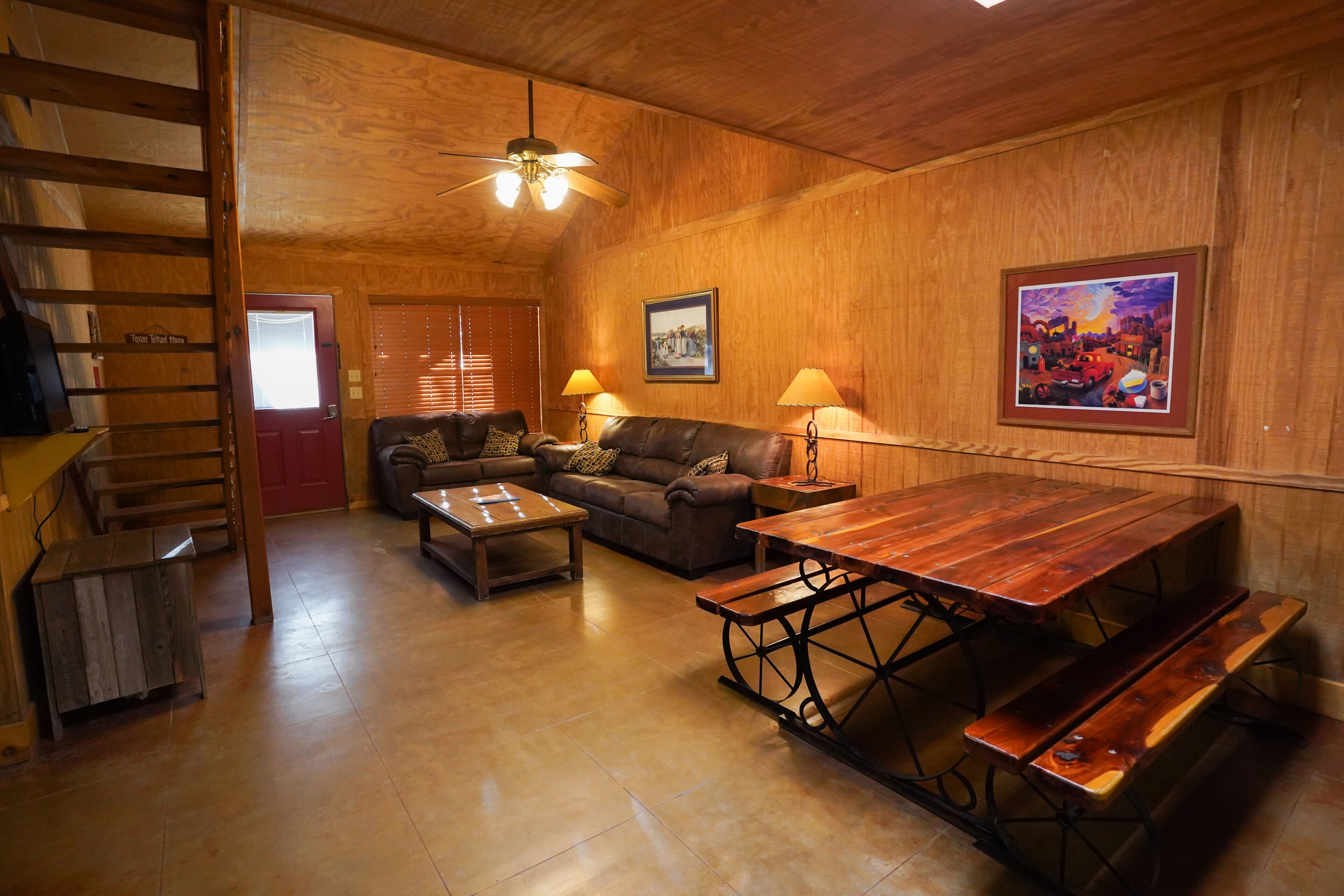 A cozy living room with a wooden ceiling, a sofa set, a wooden table with benches, and a ceiling fan.