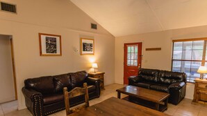 A living room with two leather sofas, a wooden coffee table, and a door with a window. - Frio Country Resort - Within walking distance to the Frio River! (Concan)