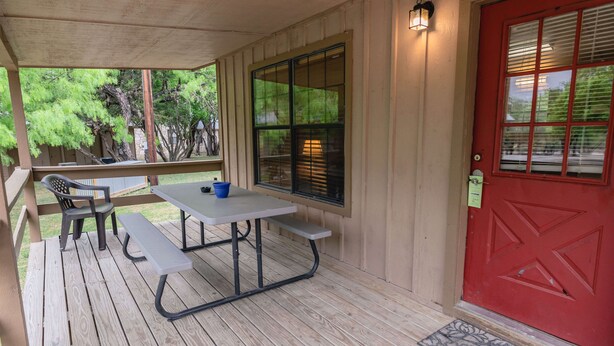 A covered outdoor area with a picnic table and benches, a red door, and a view of trees. - Frio Country Resort - Within walking distance to the Frio River! (Concan)